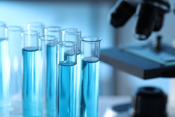 Test tubes with light blue liquid near microscope in laboratory, closeup