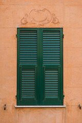 Fototapeta na wymiar Orange wall with green window on street in Liguria Italy