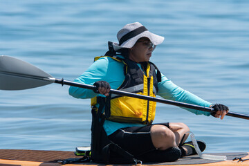 Woman in life jacket and on SUP board exercising at sea water. Special equipment such as seating...