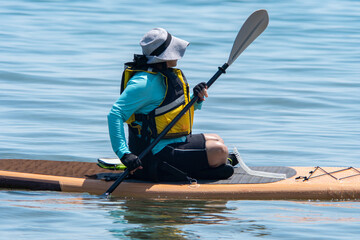 Woman sail on a SUP boards with special seating chair and wet suit and life jacket for paddling....