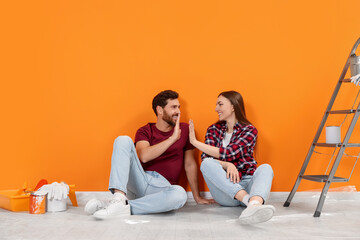 Happy man giving woman high five on floor near orange wall indoors. Interior design - Powered by Adobe