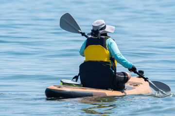 Naklejka premium Woman in life jacket and on SUP board exercising at sea water. Special equipment such as seating chare and wet suit on paddleboard. Training and sport on paddle SUP board at sunny summer day.