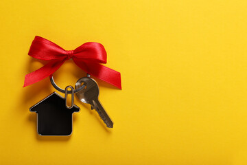 Key with trinket in shape of house and red bow on yellow background, top view. Space for text....
