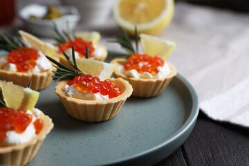 Delicious tartlets with red caviar and cream cheese served on wooden table, closeup. Space for text