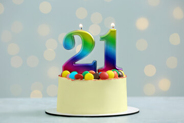 Coming of age party - 21st birthday. Delicious cake with number shaped candles on white table against blurred lights