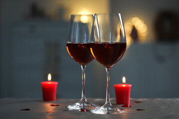 Glasses of red wine and burning candles on grey table against blurred lights, space for text. Romantic atmosphere