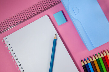 School supplies, colored pencils, eraser, pencil, ruler, penal and notebook on a pink background. School concept. School education materials, copy space, top view.