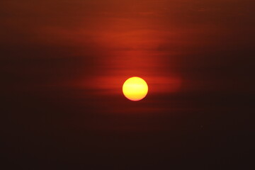 A photo of a yellow sun against a dark orange sky in the background