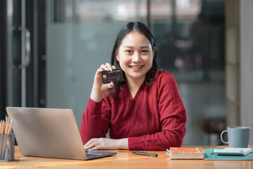 Happy Asian young woman using a laptop computer and holding a credit card for online shopping.