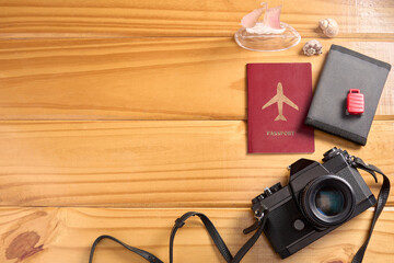 Top view of travel accessories on wooden table. Passport, camera, wallet, miniature suitcase and embarkation, and seashells. Travel planning, booking and insurance. Background with copy space.