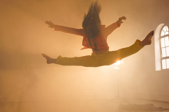 Image of biracial female modern dancer dancing in smoked interior
