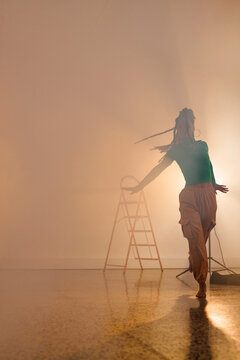 Vertical image of biracial female modern dancer dancing in smoked interior