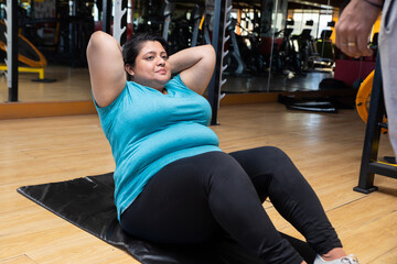 Young overweight indian woman lying doing crunches workout in gym to lose weight and burn belly fat...