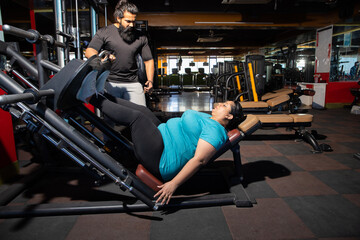 Fototapeta na wymiar Young overweight indian woman workout in gym with trainer to lose weight and burn belly fat exercise. fitness and health care