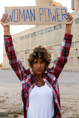 Confident African american demonstration protester looking at camera holding a woman power sign...