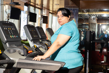 Young overweight indian woman is workout in gym to lose weight. Asian female doing cardio training and running on treadmill. Closeup.
