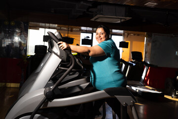 Young overweight indian woman is workout in gym to lose weight. Asian female doing cardio training on bicycle machine.