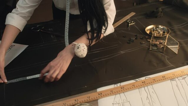 Male and female tailors work on sketch pattern on the fabric of future clothes. They use ruler, soap and buttons. Luxury designer atelier or tailoring dim studio. Fashion and hand craft concept.