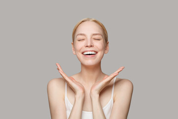 Happy blonde woman with makeup smiling isolated on grey background
