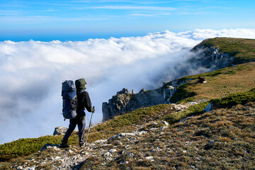 Fototapeta premium Silhouette of a man in the mountains. Successfully achieving goals. Male hiker on mountain peak with green grass looking at beautiful mountain valley at sunset against clear blue sky.. 