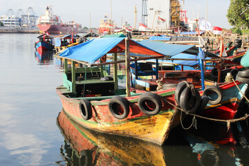 portrait of traditional fishing boats that lean on the dock beside the largest container port in...