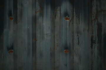 Close-up of part of a corrugated metal fence. Partially faded blue, rust.