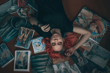 Obraz na płótnie Canvas Young redhead woman artist lying on the floor with her paintings