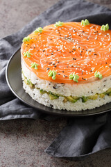 Homemade sushi cake with lightly salted salmon, avocado, soft cheese and seaweed closeup on the plate on the table. Vertical