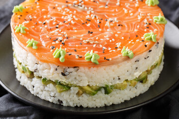 Festive sushi cake with red fish, rice, avocado, cream cheese, seaweed, sesame is decorated with wasabi close-up in a plate on the table. Horizontal