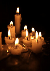 A few candles glow in the dark. Burning candles on a black background. Yellow candles. The flame burns out. Prayer for peace and tranquility. Spirituality and faith