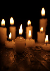 A few candles glow in the dark. Burning candles on a black background. Yellow candles. The flame burns out. Prayer for peace and tranquility. Spirituality and faith