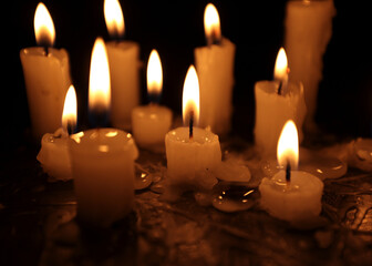 A few candles glow in the dark. Burning candles on a black background. Yellow candles. The flame burns out. Prayer for peace and tranquility. Spirituality and faith