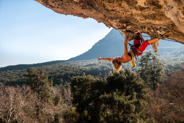 A young rock climber on an overhanging cliff. The climber climbs the rock. The girl is engaged in...