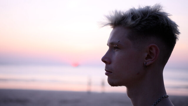 Thoughtful guy looks into the distance on the beach during sunset