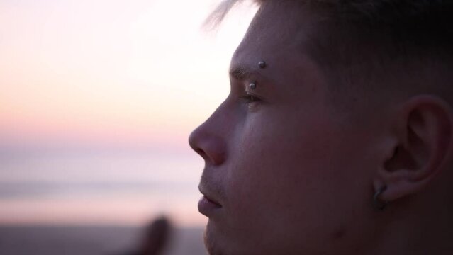 Thoughtful guy looks into the distance on the beach during sunset