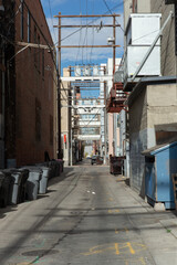 Dirty downtown urban city alley or alleyway off street showing garbage cans litter and dumpsters and underground utility facilities markers during the day with a blue sky