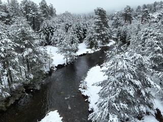 An aerial view of a frozen river flowing through snow-covered forests on a cloudy sunset sky background.