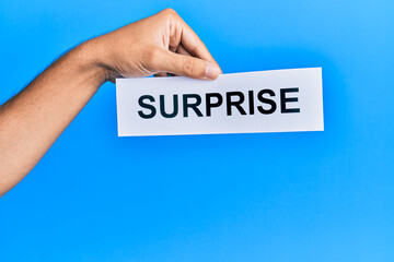 Hand of caucasian man holding paper with surprise word over isolated blue background