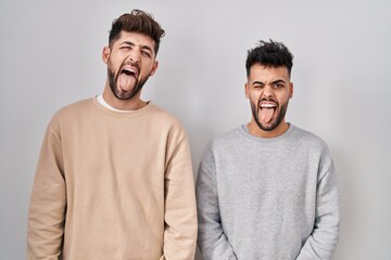 Young homosexual couple standing over white background sticking tongue out happy with funny expression. emotion concept.