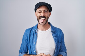 Hispanic man with beard standing over isolated background sticking tongue out happy with funny expression. emotion concept.