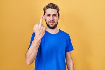 Hispanic man with beard standing over yellow background showing middle finger, impolite and rude...