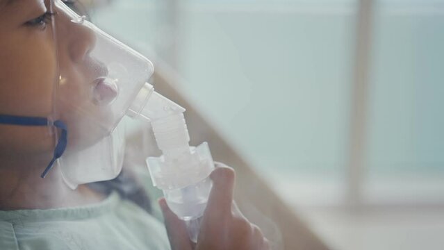 Asian girl having an oxygen mask and breathing through a nebulizer at the hospital.