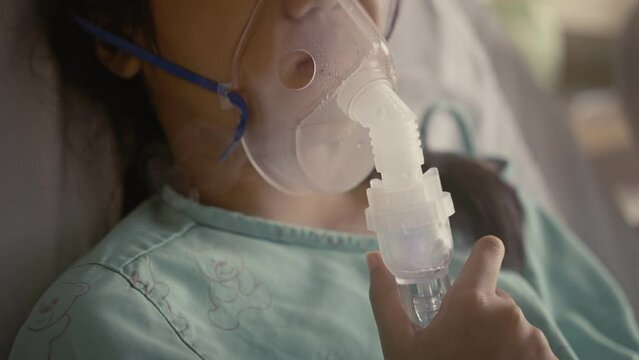 Asian girl having an oxygen mask and breathing through a nebulizer at the hospital.