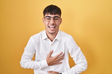 Young hispanic man standing over yellow background smiling and laughing hard out loud because funny...