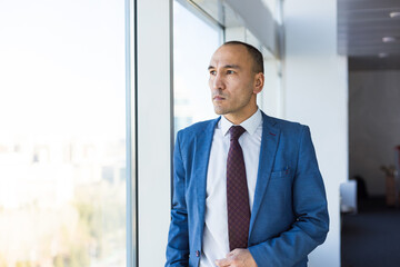 Portrait of a business young successful man in a modern office standing by the window against the backdrop of the city