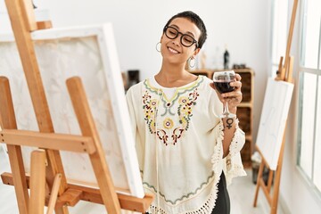 Young hispanic woman drinking wine drawing at art studio