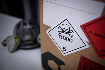 White toxic symbol and red flammable symbol on a box with a mask in the background.