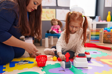 Teacher and student playing supermarket game sitting on floor at kindergarten