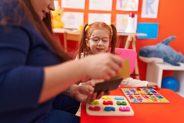 Fototapeta premium Teacher and student playing with maths puzzle game looking cards at kindergarten