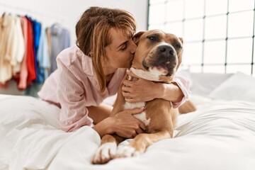 Young caucasian woman hugging and kissing dog lying on bed at bedroom